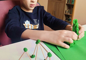 Chłopiec tworzy konstrukcje z wykałaczek i ciastoliny.