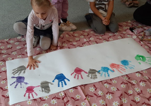 Dzieci z grupy 5 odciskają swoje dłonie na dużym plakacie.