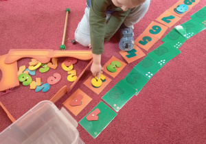 Chłopiec łowi wędką cyfry i układa na podanym wzorze.