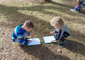 Chłopcy szkicują drzewa w ogrodzie.