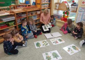 Nauczyciel i dzieci oglądają ilustracje drzew.