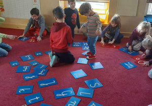 Dzieci wyszukują litery na dywanie.