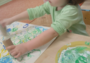 Dziewczynka tworzy obraz z użyciem stempli z rolki papierowej.