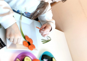 Dziewczynka układa kompozycję z owoców i warzyw.