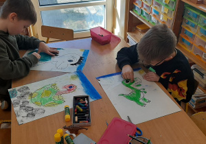 Dzieci kolorują pastelami dinozaury.