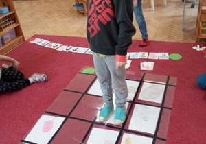 Kodowanie na dywanie - chłopiec porusza się po macie do kodowania według podanego algorytmu ułożonego przez kolegę.