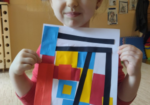 Dziewczynka prezentuje swoją pracę inspirowaną twórczością Pieta Mondrian.