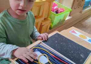 Chłopiec tworzy obraz ze sznurków.