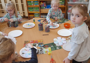 Dzieci naklejają elementy papierowe na mandalę.