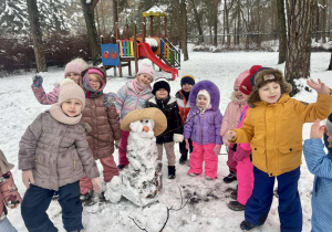 Dzieci lepią bałwana w ogrodzie.