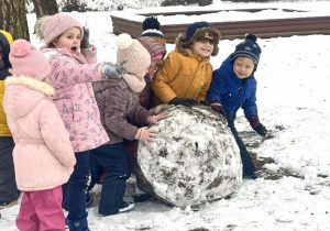 Dzieci toczą śniegową kulę.