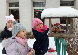 Dziewczynki wsypują ziarno do karmnika dla ptaków.
