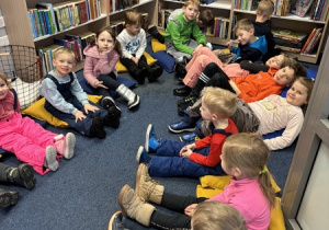 Dzieci siedzą na dywanie w bibliotece.