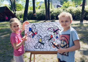 Chłopiec i dziewczynka kolorują witraż mazakami.