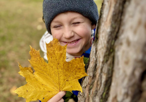 Chłopiec pozuje z liściem w ogrodzie.