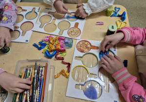 Dzieci ozdabiają różnymi materiałami kształty lupy.