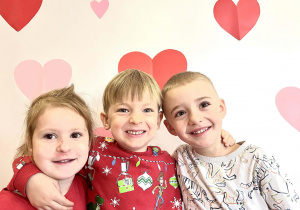 Dzieci pozują do zdjęcia na tle serduszek.