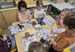 Dzieci młodsze wykonują bałwanka z wykorzystaniem worka strunowego i białych kartek.