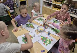 Dzieci ozdabiają kontur choinki kółeczkami i gwiazdkami.