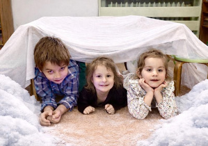 Dzieci budują igloo z firanek.