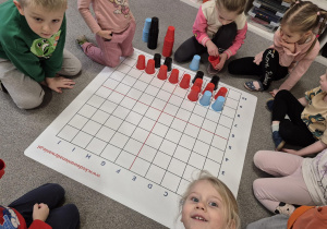 Dzieci układają na macie z kolorowych kubeczków autobus do instrukcji wierszowanej.