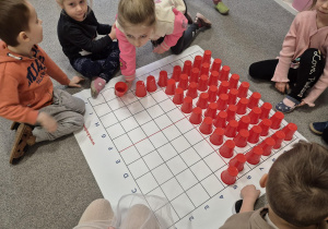 Dzieci układają na macie z kolorowych kubeczków apteczkę do instrukcji wierszowanej.