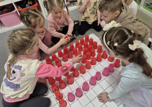 Dzieci układają na macie z kolorowych kubeczków apteczkę.