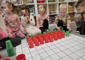 Dzieci układają na macie z kolorowych kubeczków arbuza do instrukcji wierszowanej.