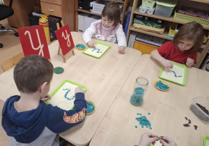 Dzieci rysują litery wg wzoru na kaszy.