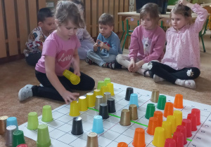 Dzieci kodują na macie z kolorowych kubeczków.