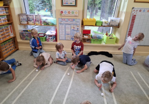 Dzieci dmuchają piłeczki po wyznaczonym torze.