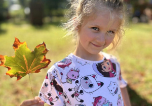 Dziewczynka w ogrodzie pozuje z jesiennym listkiem.