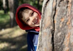 Chłopiec uśmiecha się zza drzewa w parku.