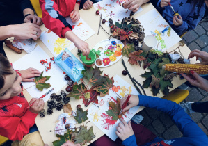 Dzieci podczas spotkania integracyjnego z rodzicami  odciskają na płótnie malarskim pomalowane farbami dary jesieni.
